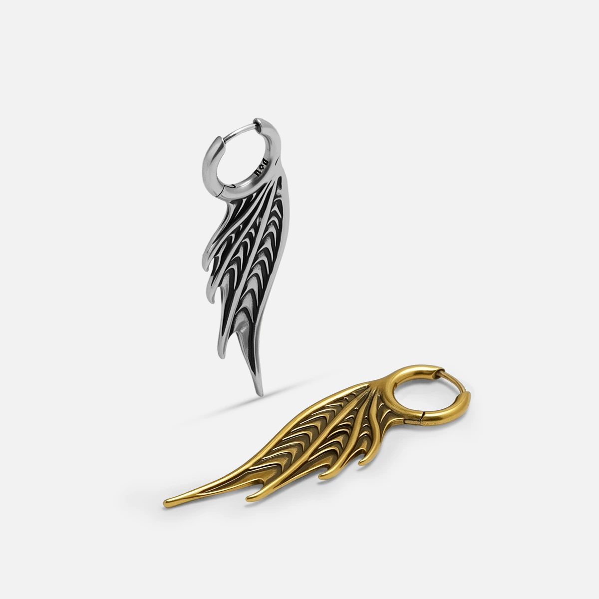 Silver and gold Spined Wing Earrings shown together, featuring long ribbed wing forms, hoop closures, and sharp fin-like silhouettes.