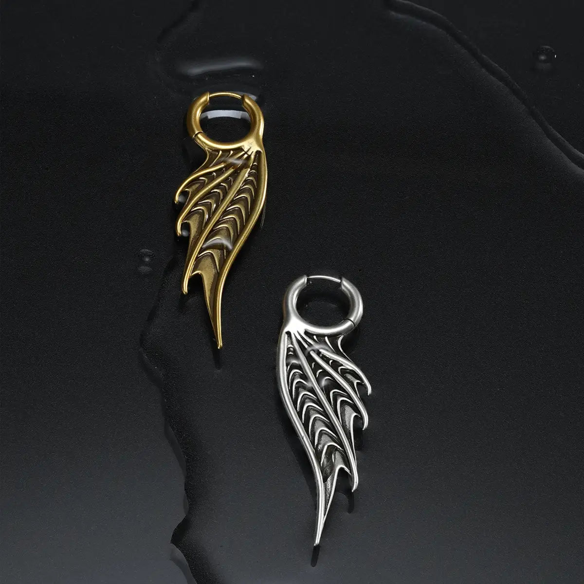 Silver and gold Spined Wing Earrings displayed on a dark wet surface, featuring long fin-like drops and sculptural gothic details.