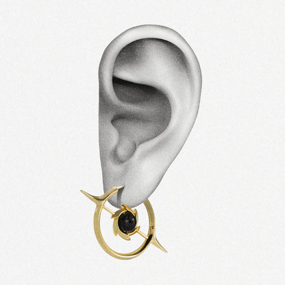 Gold-tone hoop earring with star motif and dark round stone shown worn on an ear