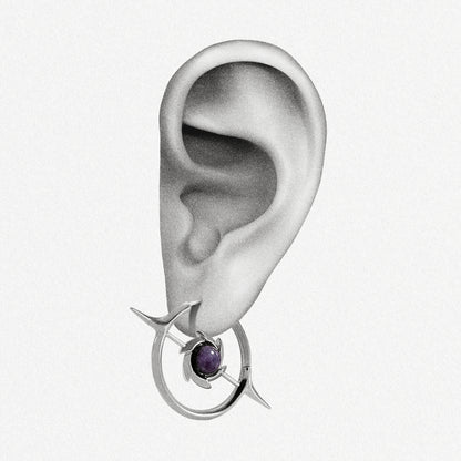 Silver-tone hoop earring with star motif and round purple stone shown worn on an ear