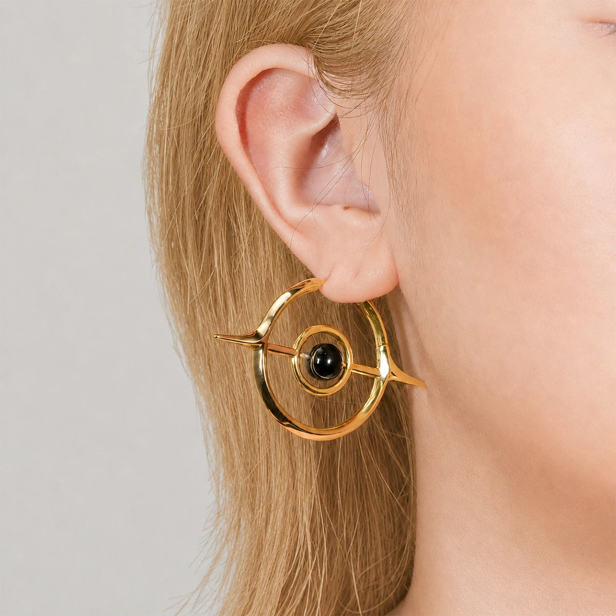 Gold-tone Stellar Grace hoop earring with spike accents and a black stone, worn on a model's ear