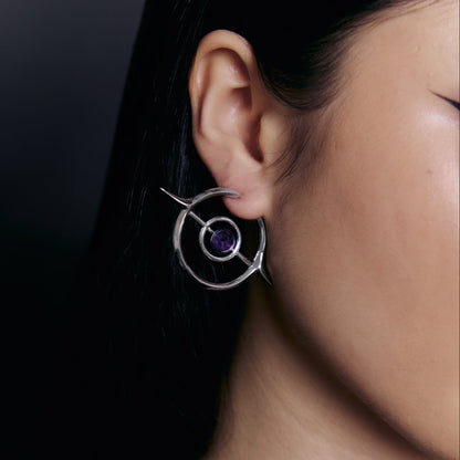 Silver-tone Stellar Grace hoop earring with spike details and a purple stone, worn on a model's ear