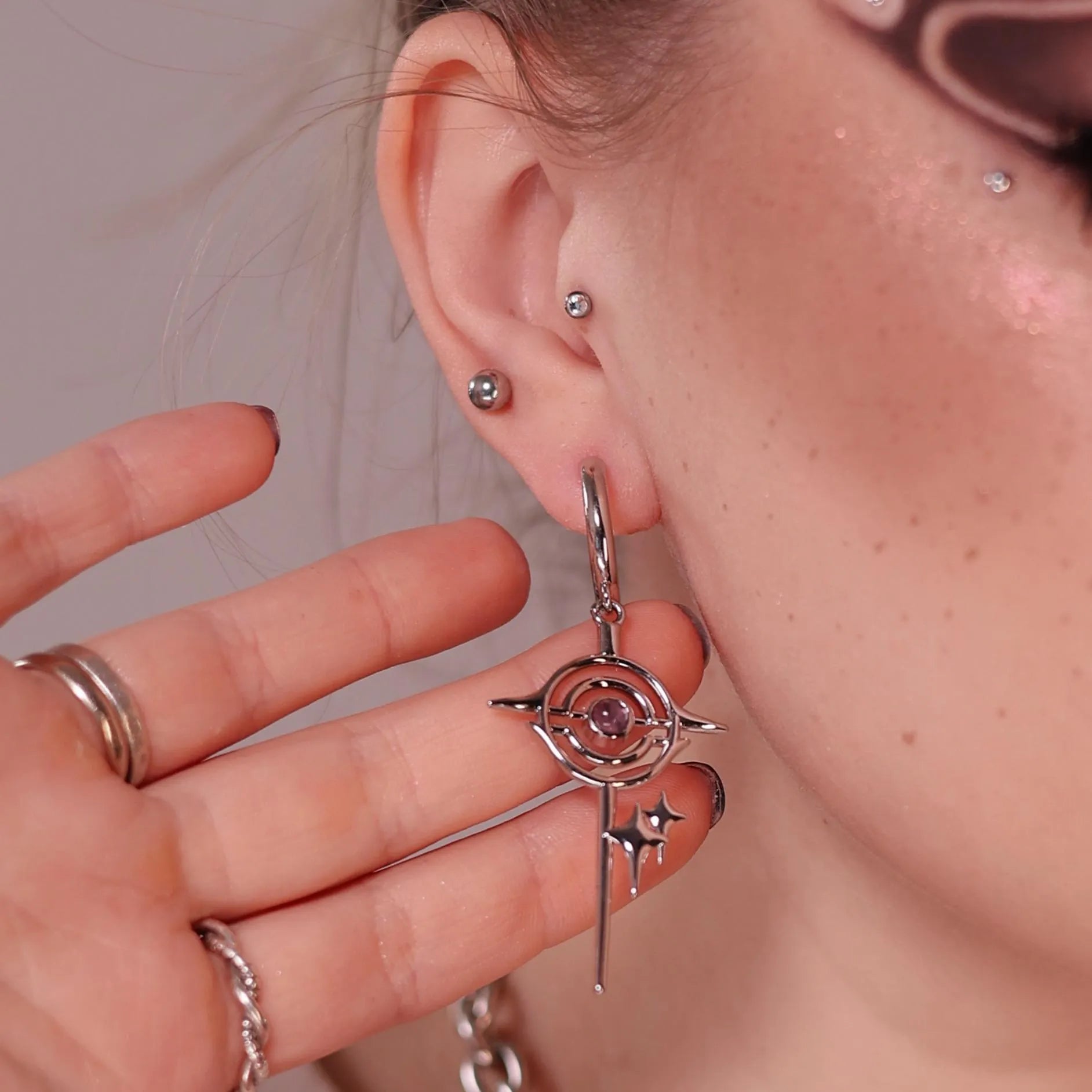 Model wearing the silver Stellar Path Earrings with amethyst center, orbital frame, pointed star drop, and celestial-inspired gothic styling.