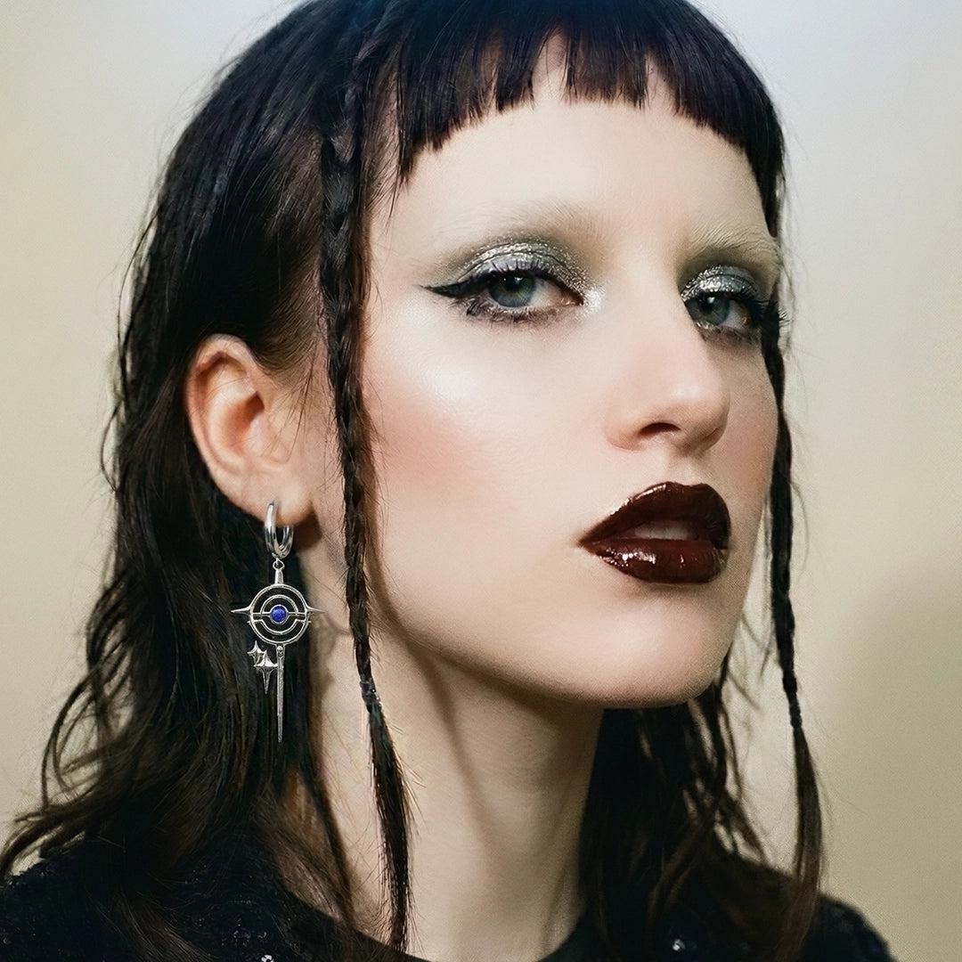 Close-up of a model wearing a silver-tone drop earring with a circular star motif and blue stone