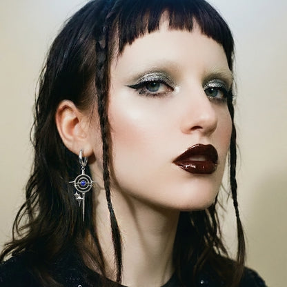 Close-up of a model wearing a silver-tone drop earring with a circular star motif and blue stone