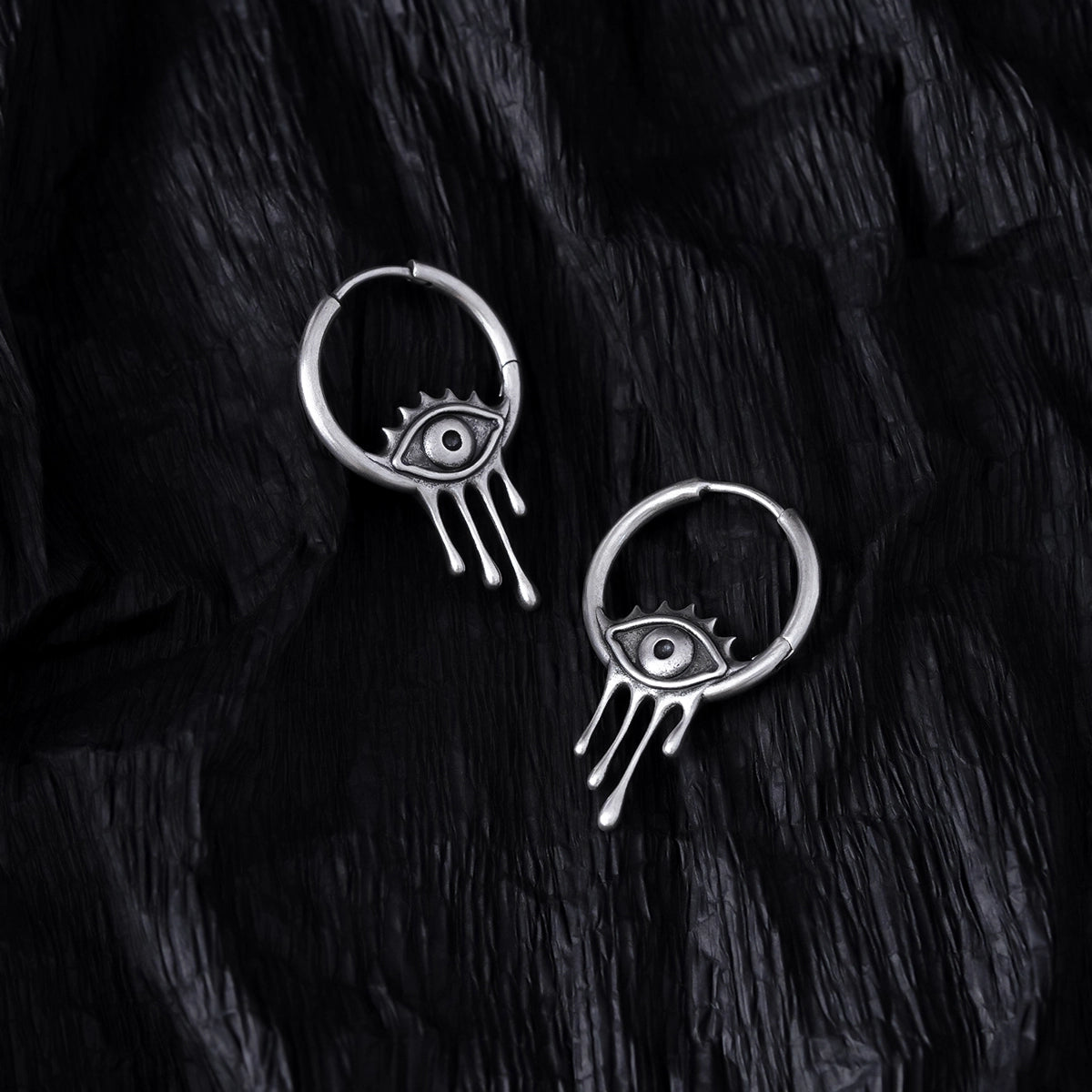 Pair of silver Surrealist Eye hoop earrings displayed on black feathers