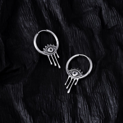 Pair of silver Surrealist Eye hoop earrings displayed on black feathers