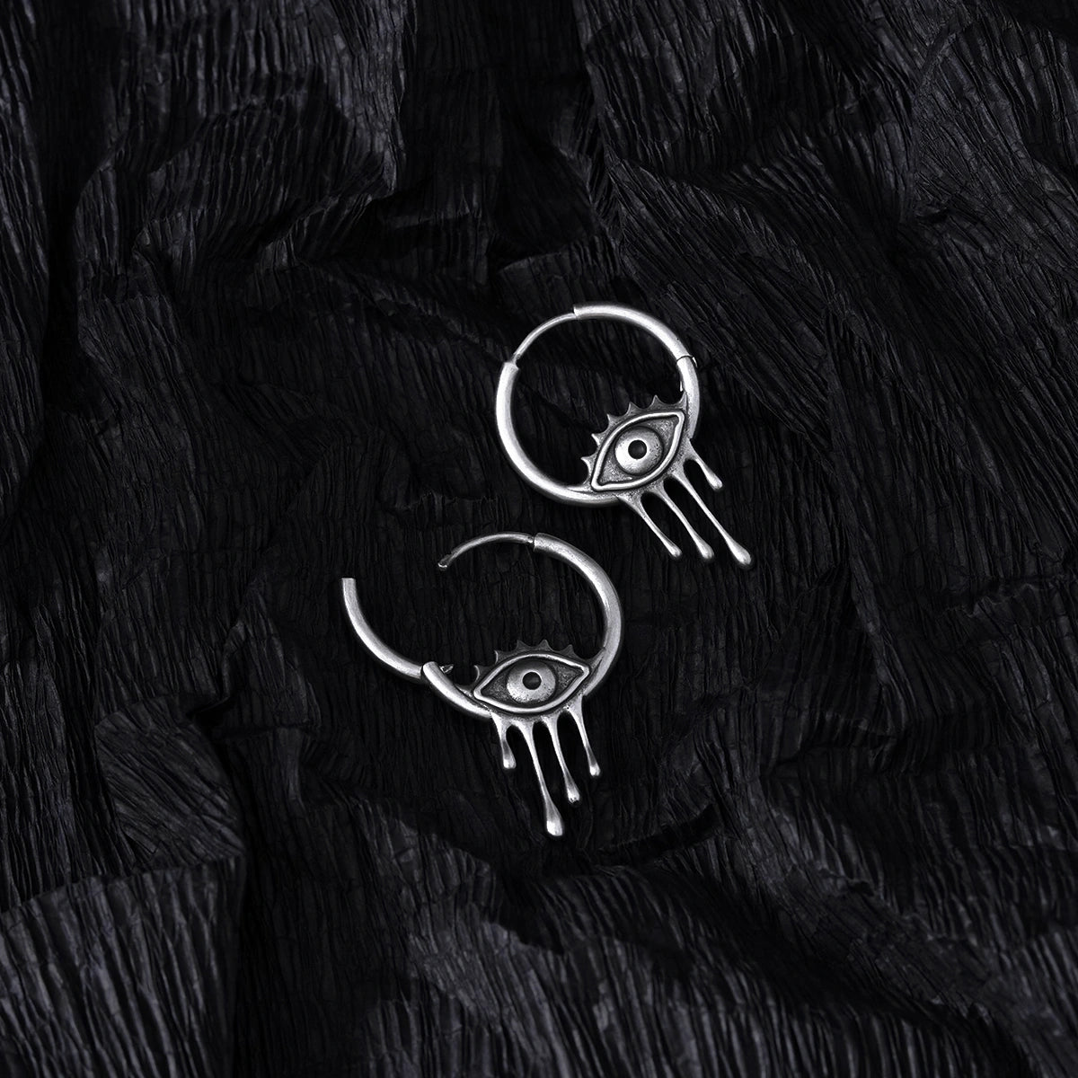 Silver Surrealist Eye hoop earrings shown open and closed on black feathers