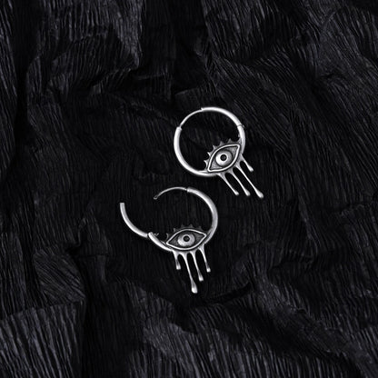 Silver Surrealist Eye hoop earrings shown open and closed on black feathers