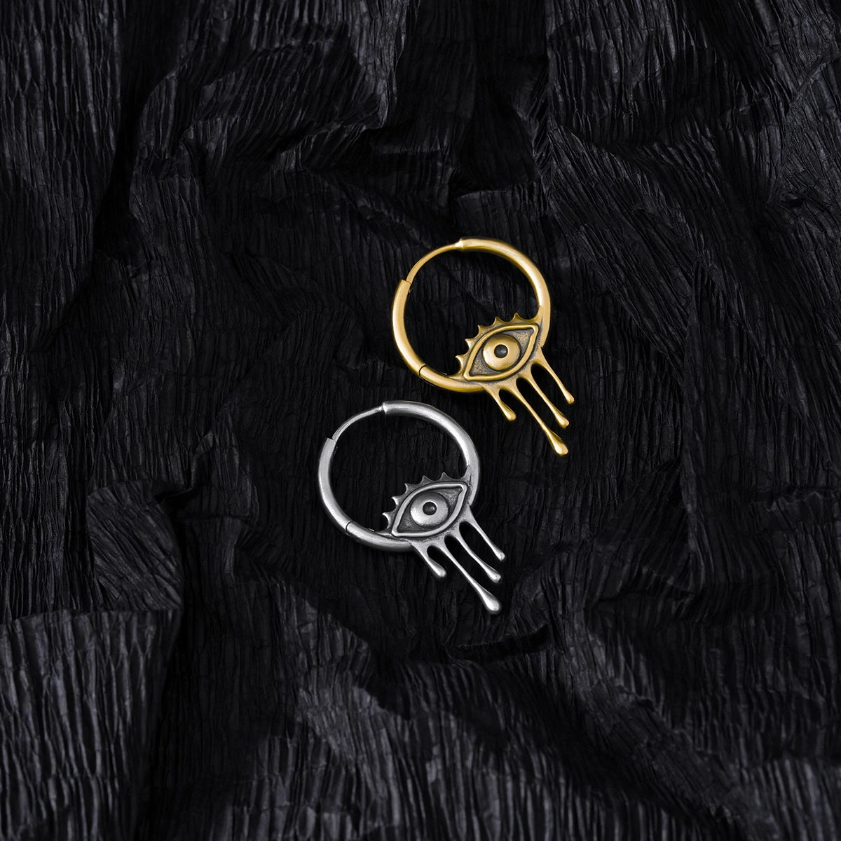 Silver and gold Surrealist Eye hoop earrings displayed on black feathers