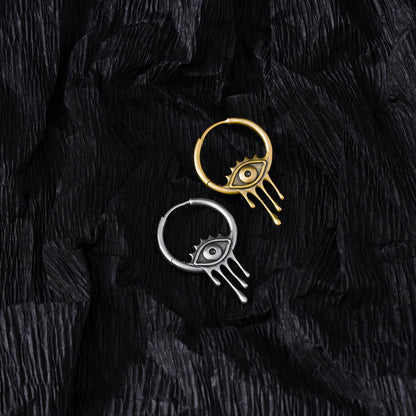 Silver and gold Surrealist Eye hoop earrings displayed on black feathers