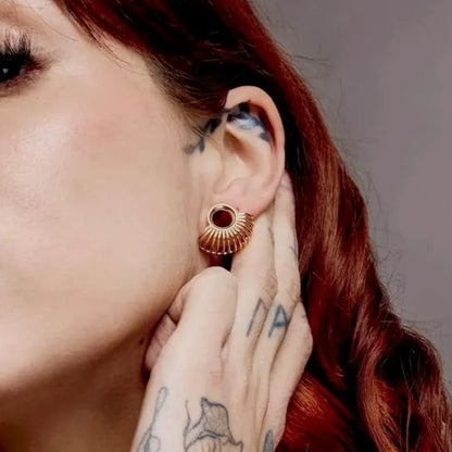 Close up of an ear wearing a gold-tone radiance tunnel with fanned rays, worn with tattooed fingers nearby