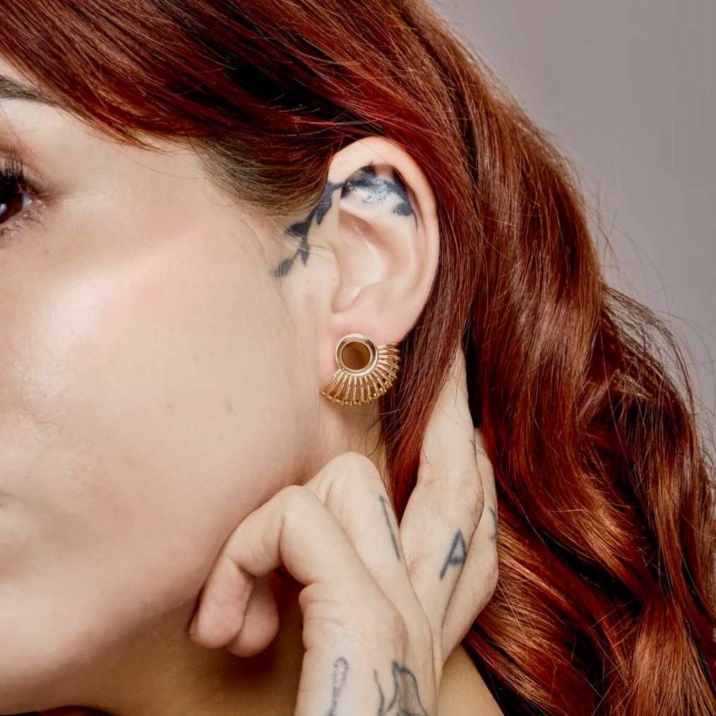 Side profile of a model with red hair wearing a gold-tone sunburst tunnel earring