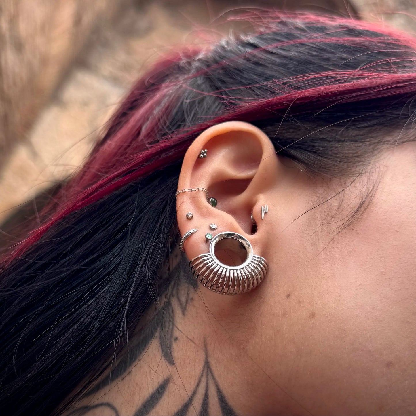 Close-up of silver Symmetrical Radiance tunnel worn with multiple ear piercings
