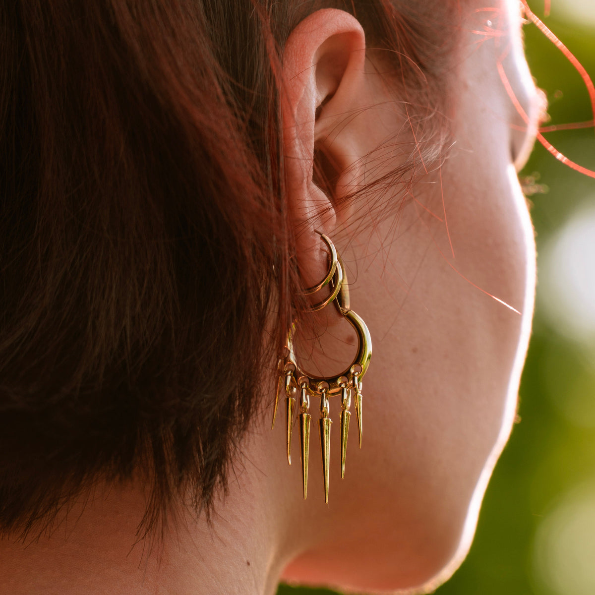 Gold-tone Tapered Chic hoop earring worn outdoors, viewed from behind with five pointed drops
