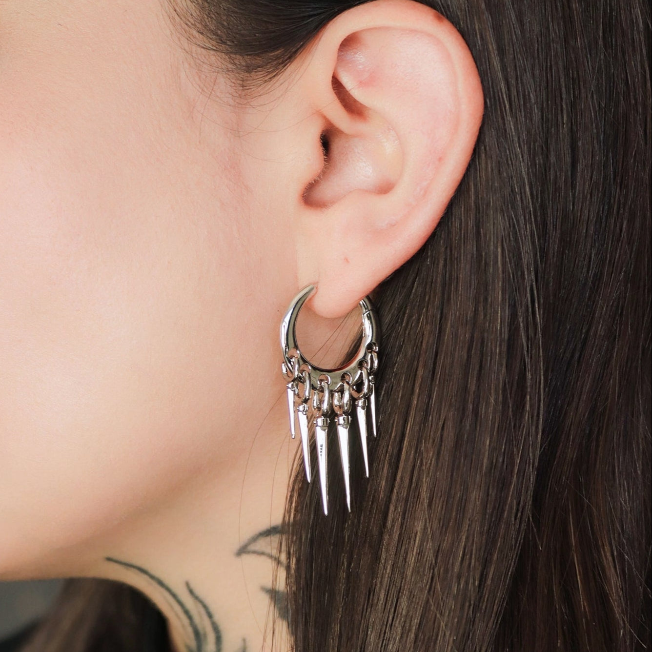 Silver-tone tapered chic hoop earring with dangling spike charms worn on a close-up ear view