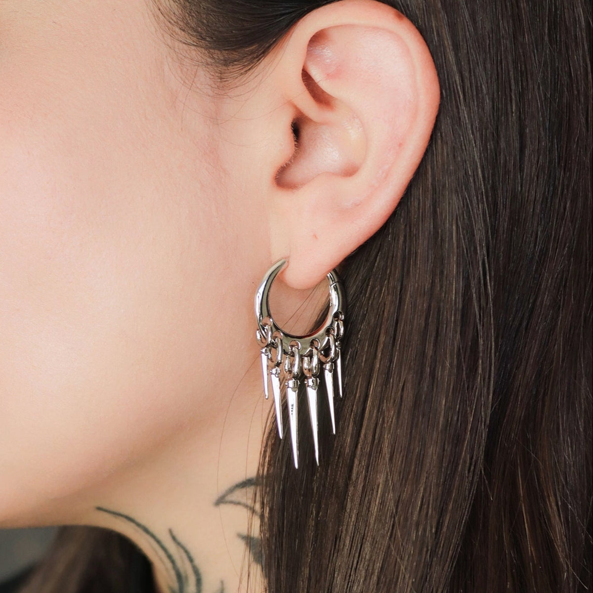 Silver-tone tapered chic hoop earring with dangling spike charms worn on a close-up ear view