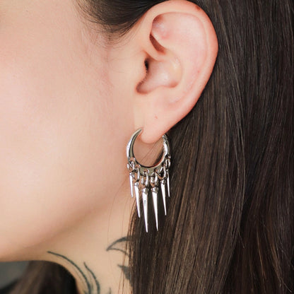 Silver-tone tapered chic hoop earring with dangling spike charms worn on a close-up ear view