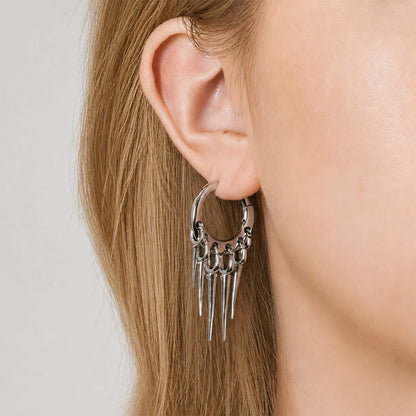 Close-up side view of a silver-tone hoop earring with tapered spike drops worn on the ear