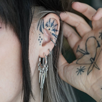 Silver-tone tapered spike hoop earring worn alongside multiple ear piercings and a hand near the hair