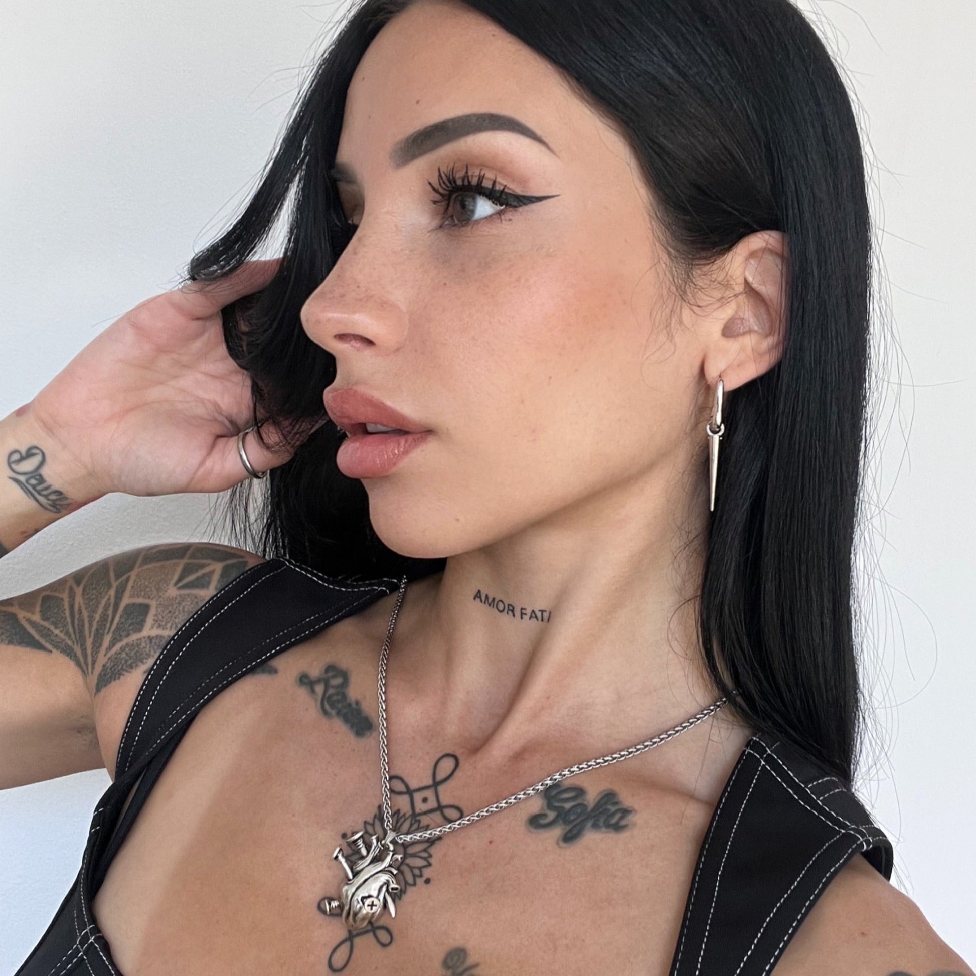 Silver-tone tapered edge earring worn on a hoop, seen in a close-up side view alongside a layered necklace