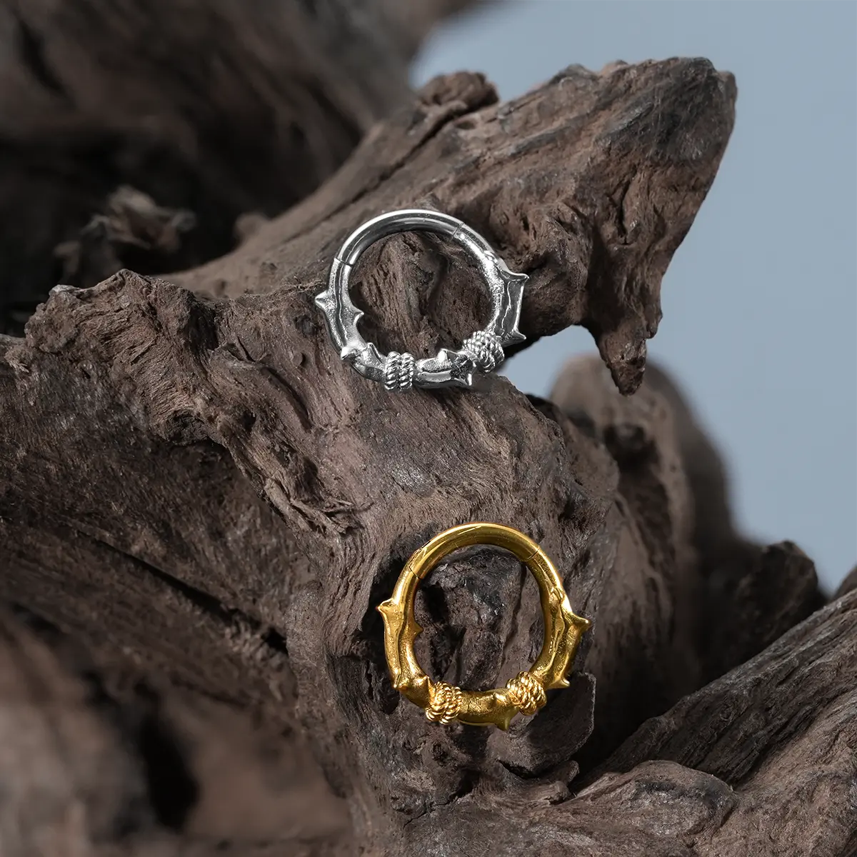 Thorn Bramble Clicker in gold and silver displayed on driftwood with dark woodland styling