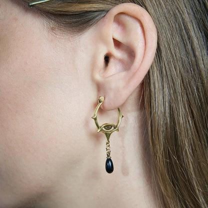 Gold-tone Thorned Gaze Hoop Earrings worn in a downward-looking portrait, highlighting the open thorned frames and black teardrop drops.