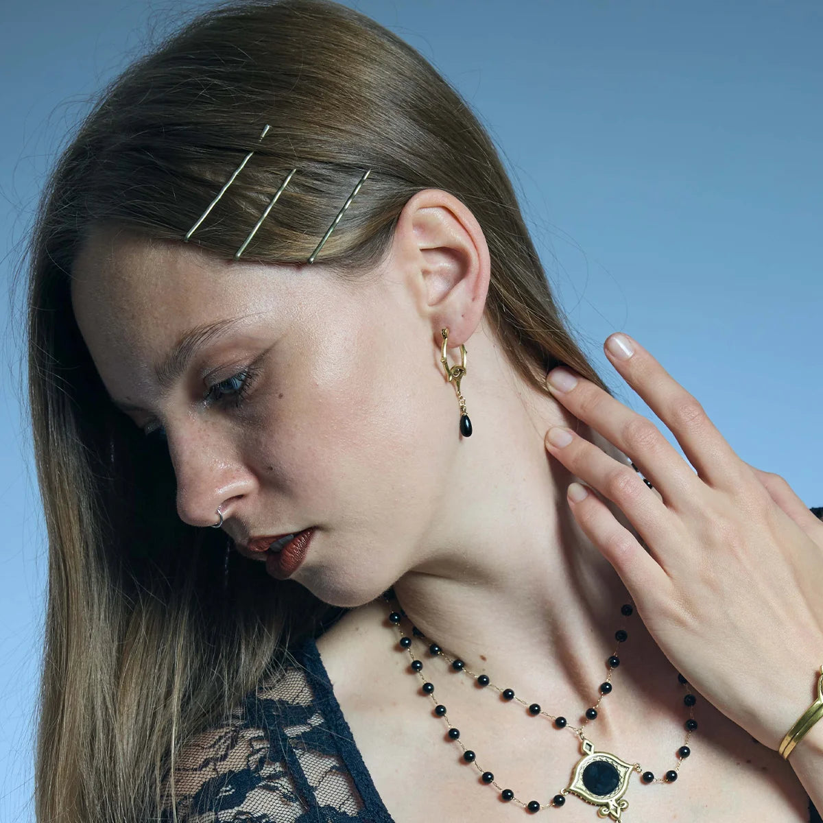 Close side portrait of a gold-tone Thorned Gaze Hoop Earring, highlighting the thorned open frame, engraved eye detail, and black teardrop drop.