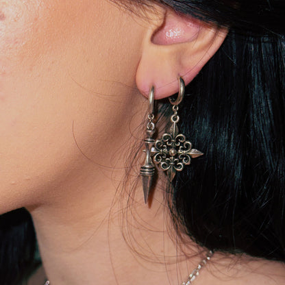 Close-up of a model wearing dark-toned spear and filigree cross drop earrings on a huggie hoop
