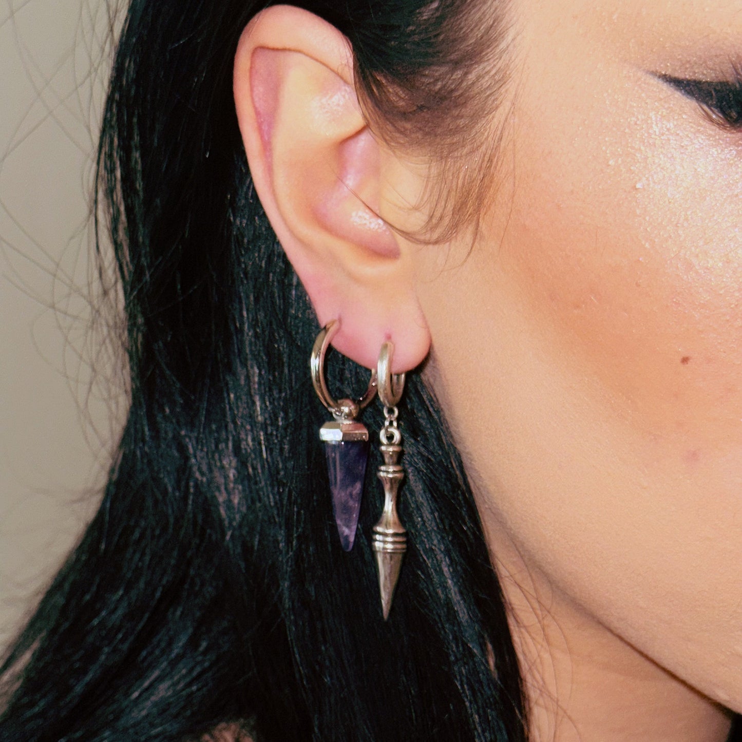 Model wearing layered hoop earrings with a purple stone charm and a silver-tone spear pendant