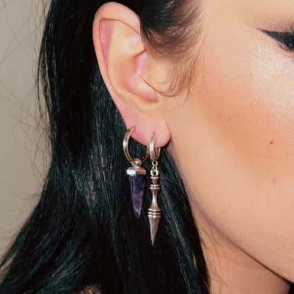 Model wearing layered hoop earrings with a purple stone charm and a silver-tone spear pendant