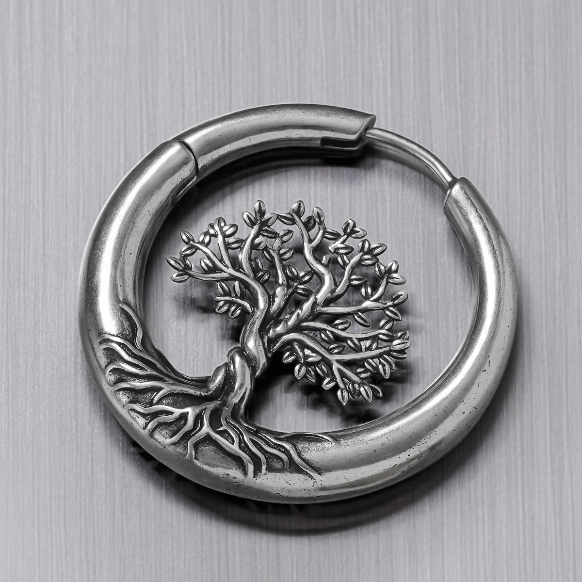 Close-up of a silver-tone hoop earring with detailed tree of life and roots design