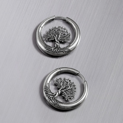 Pair of silver-tone tree of life hoop earrings laid flat on a metallic surface