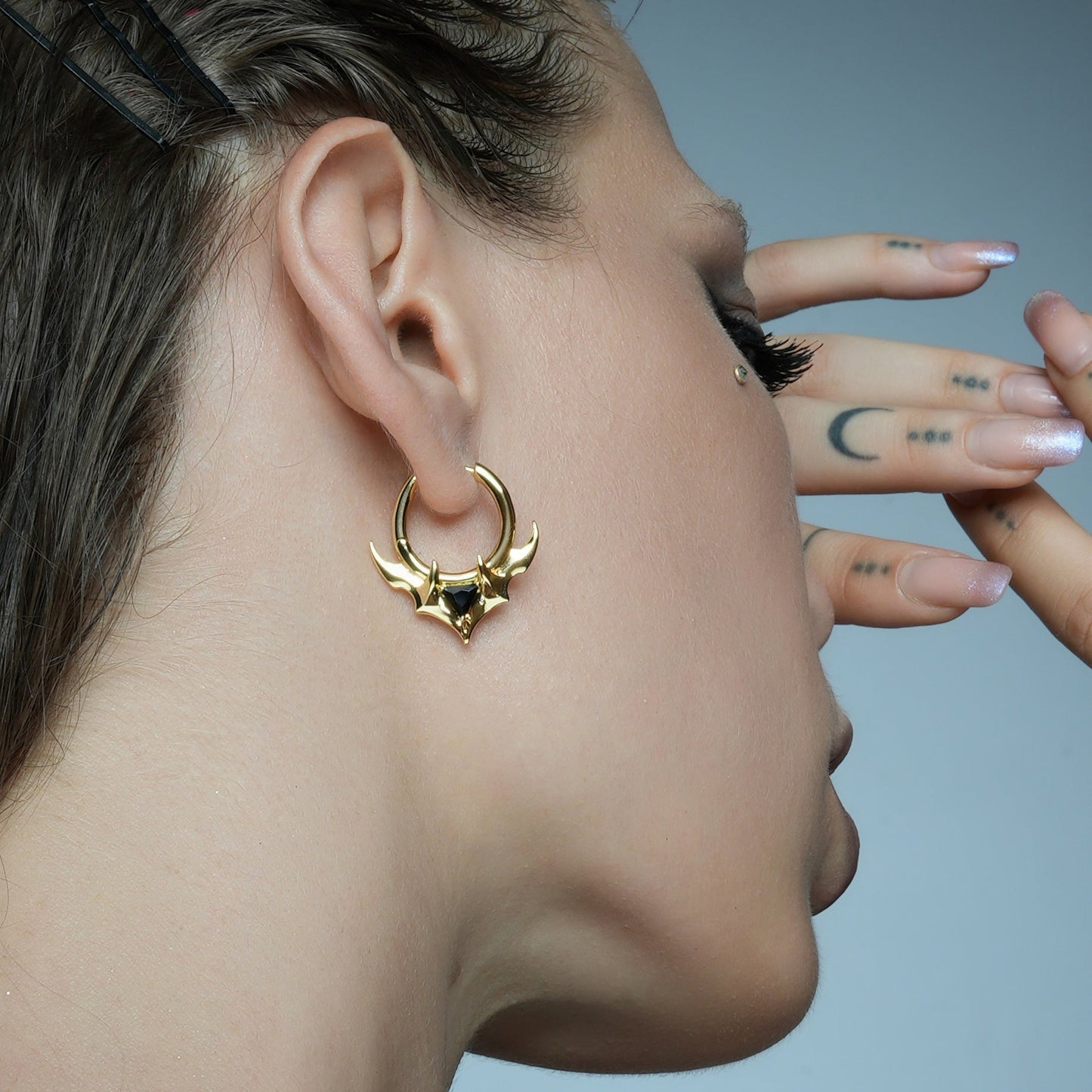 Model tilts the head to display a gold-tone hoop earring with horn details and a black stone