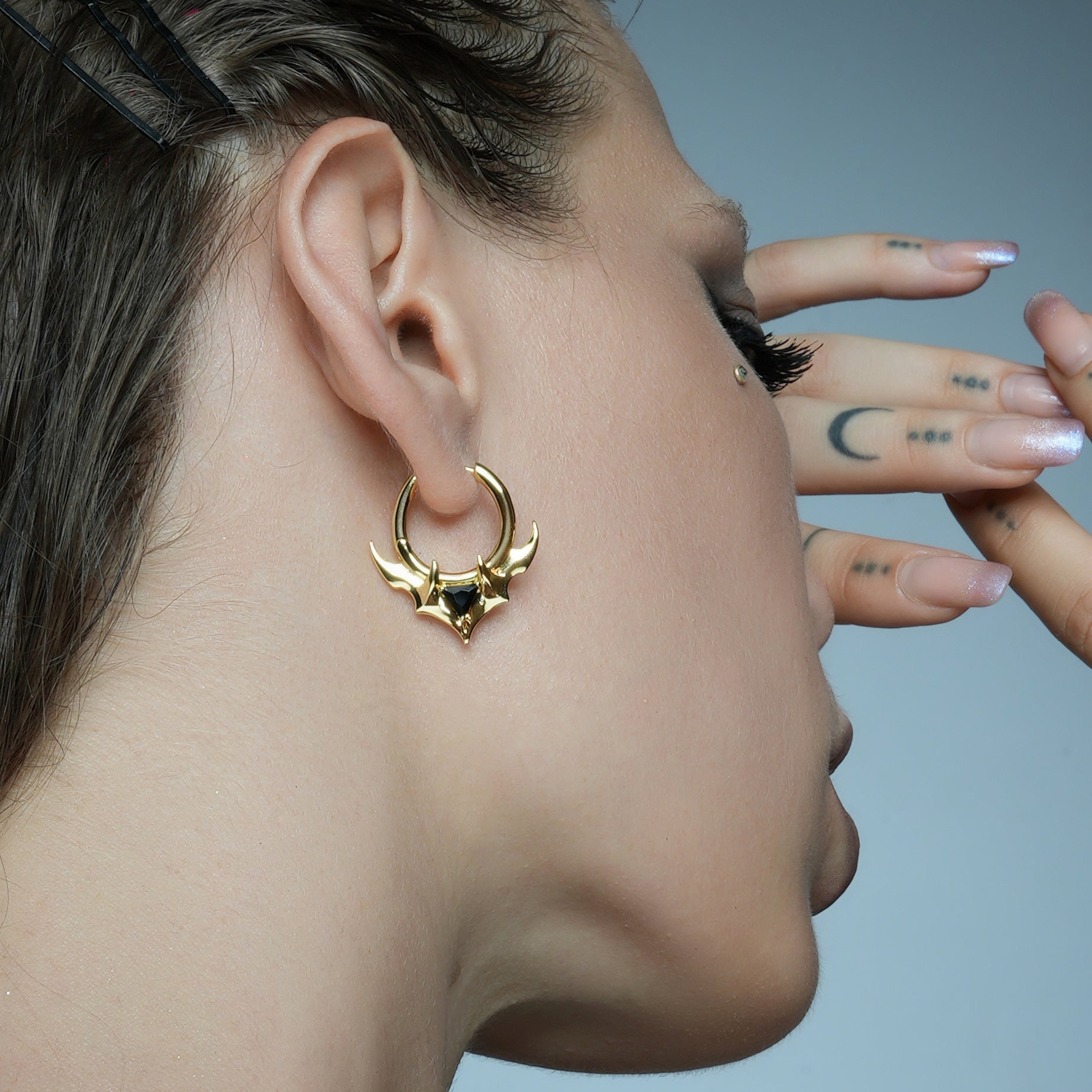 Model tilts the head to display a gold-tone hoop earring with horn details and a black stone