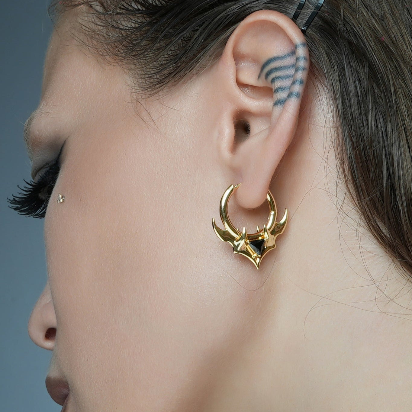 Close-up of a model wearing a gold-tone hoop earring featuring horn shapes and a black stone