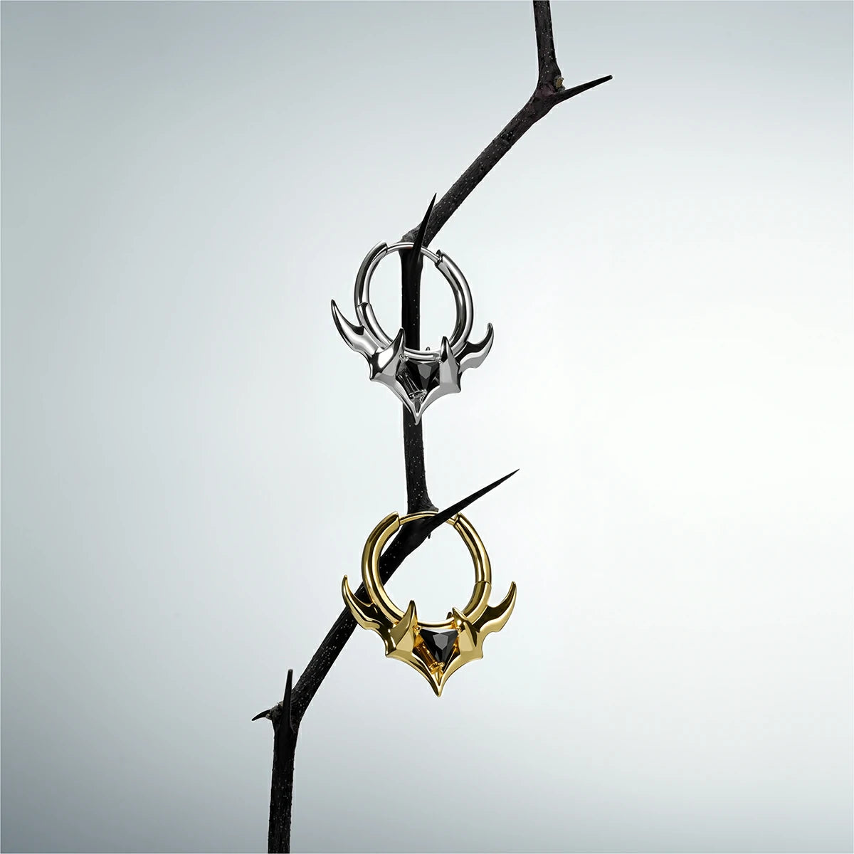 Silver and gold Trident Crest stone hoop earrings hanging from a dark branch