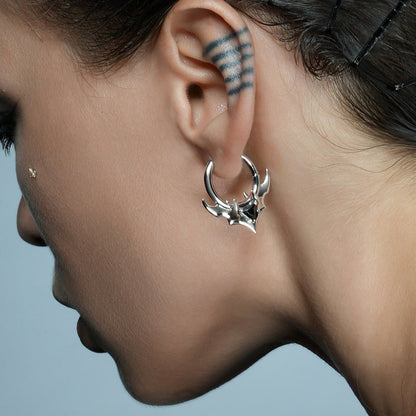 Close-up of a model wearing a silver-tone hoop earring with horn accents and a black stone