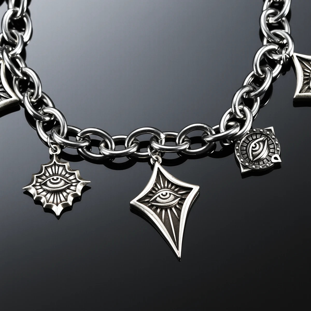 Close-up of the antiqued silver-tone Unblinking Procession Bracelet showing radiating and pointed eye charms on a dark reflective surface.