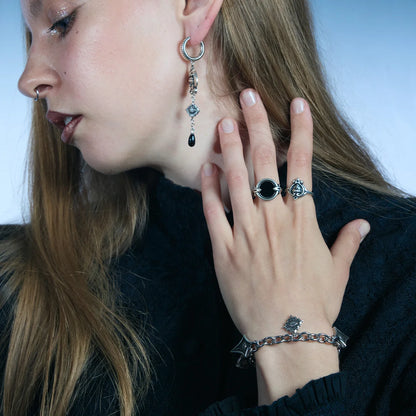 Side portrait showing an antiqued silver-tone Unblinking Procession Bracelet with eye charms hanging from the solid link chain.