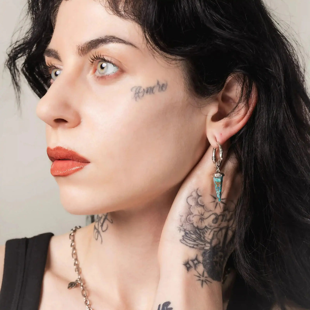 Unearthed Spike Earrings in 925 sterling silver, worn in side profile by a tattooed brunette with the turquoise spike clearly