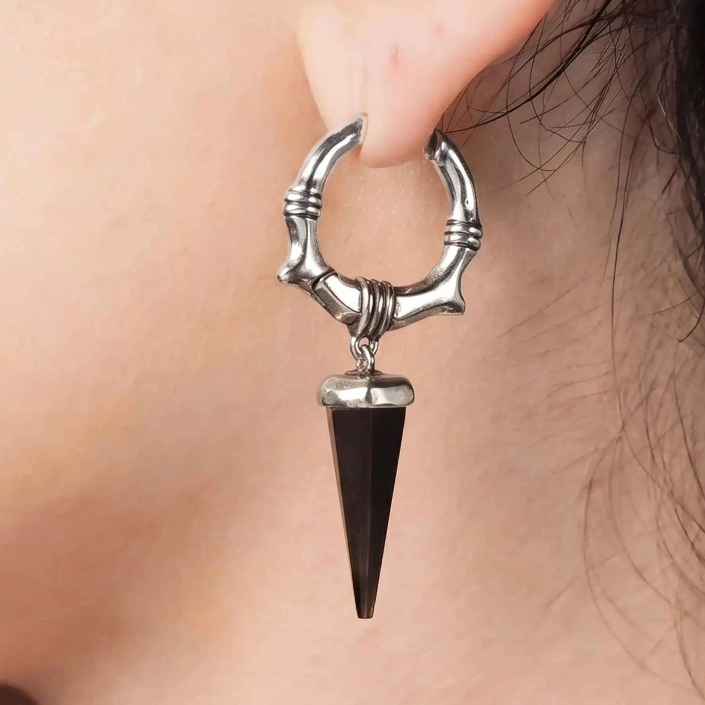 Model wearing the silver Unearthed Spike Earrings with black obsidian spike drops, showing the sharp gothic silhouette and bone-textured hoop design.
