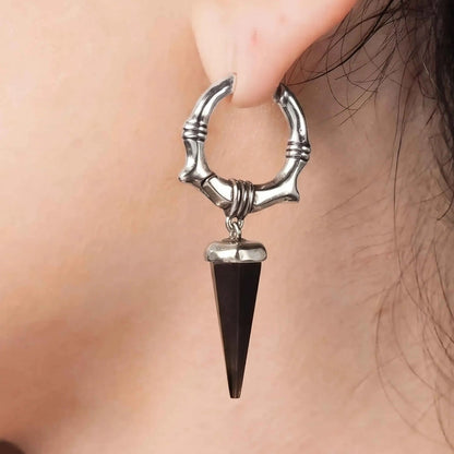 Model wearing the silver Unearthed Spike Earrings with black obsidian spike drops, showing the sharp gothic silhouette and bone-textured hoop design.