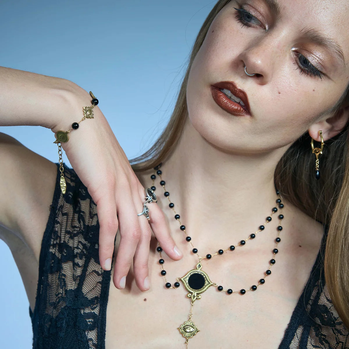 Gold-tone Unseen Orbit Bracelet worn in a styled portrait with the eye-shaped links and black obsidian beads visible around the wrist.