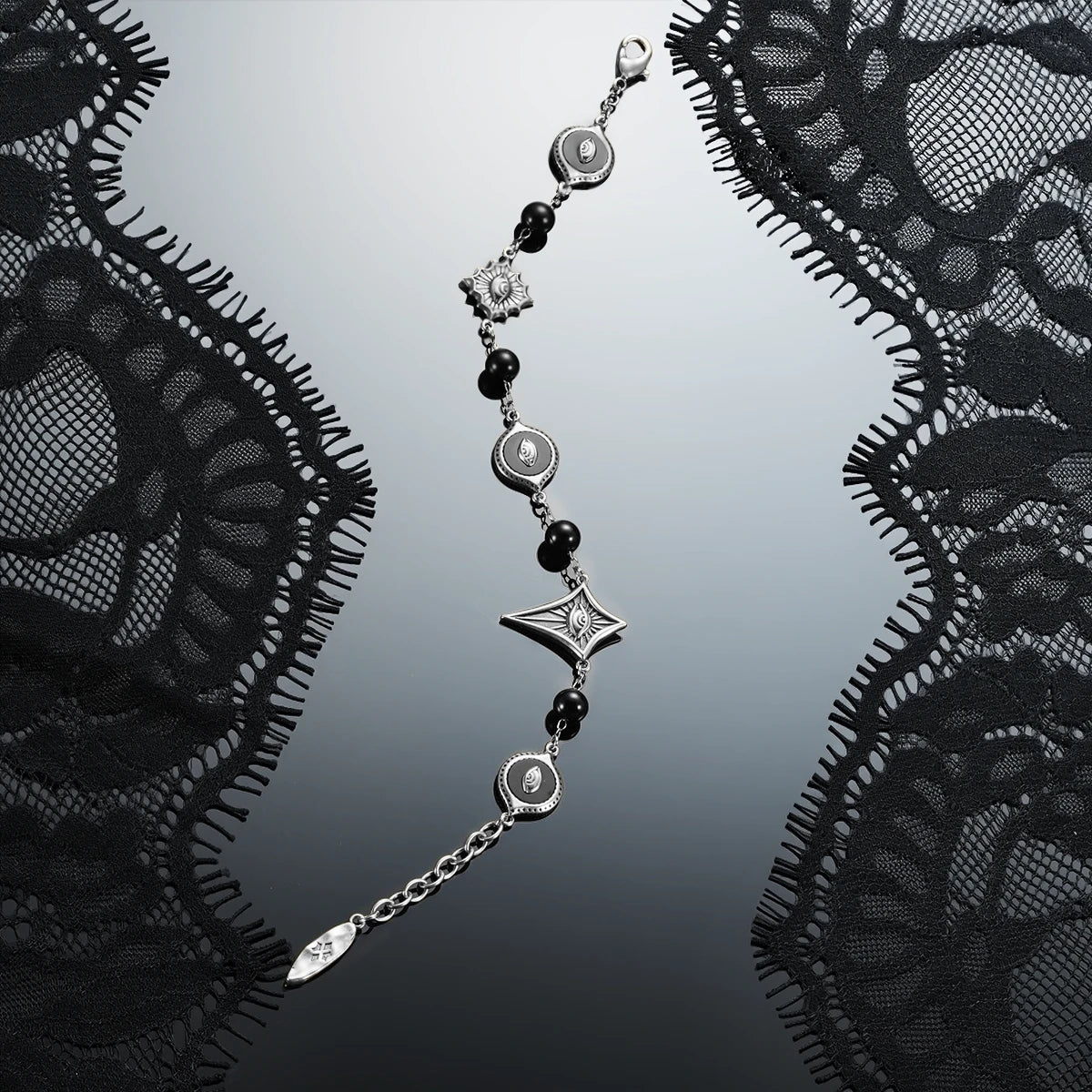 Antiqued silver-tone Unseen Orbit Bracelet displayed diagonally against black lace on a dark reflective surface.