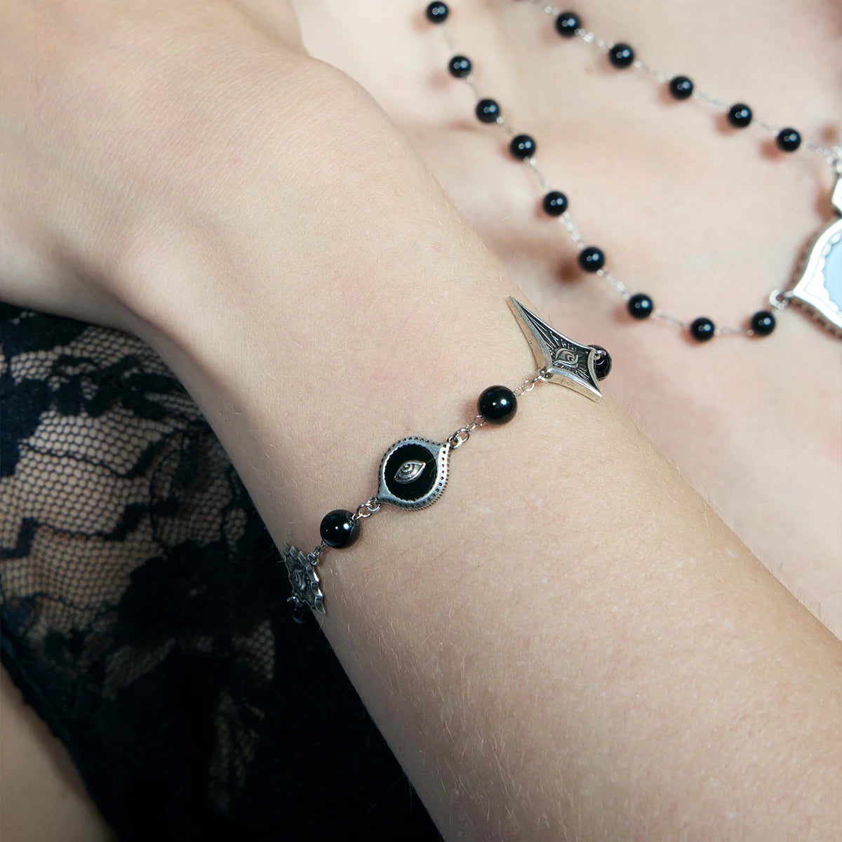 Close-up of an antiqued silver-tone Unseen Orbit Bracelet worn flat against the wrist with black obsidian beads and eye-shaped links.