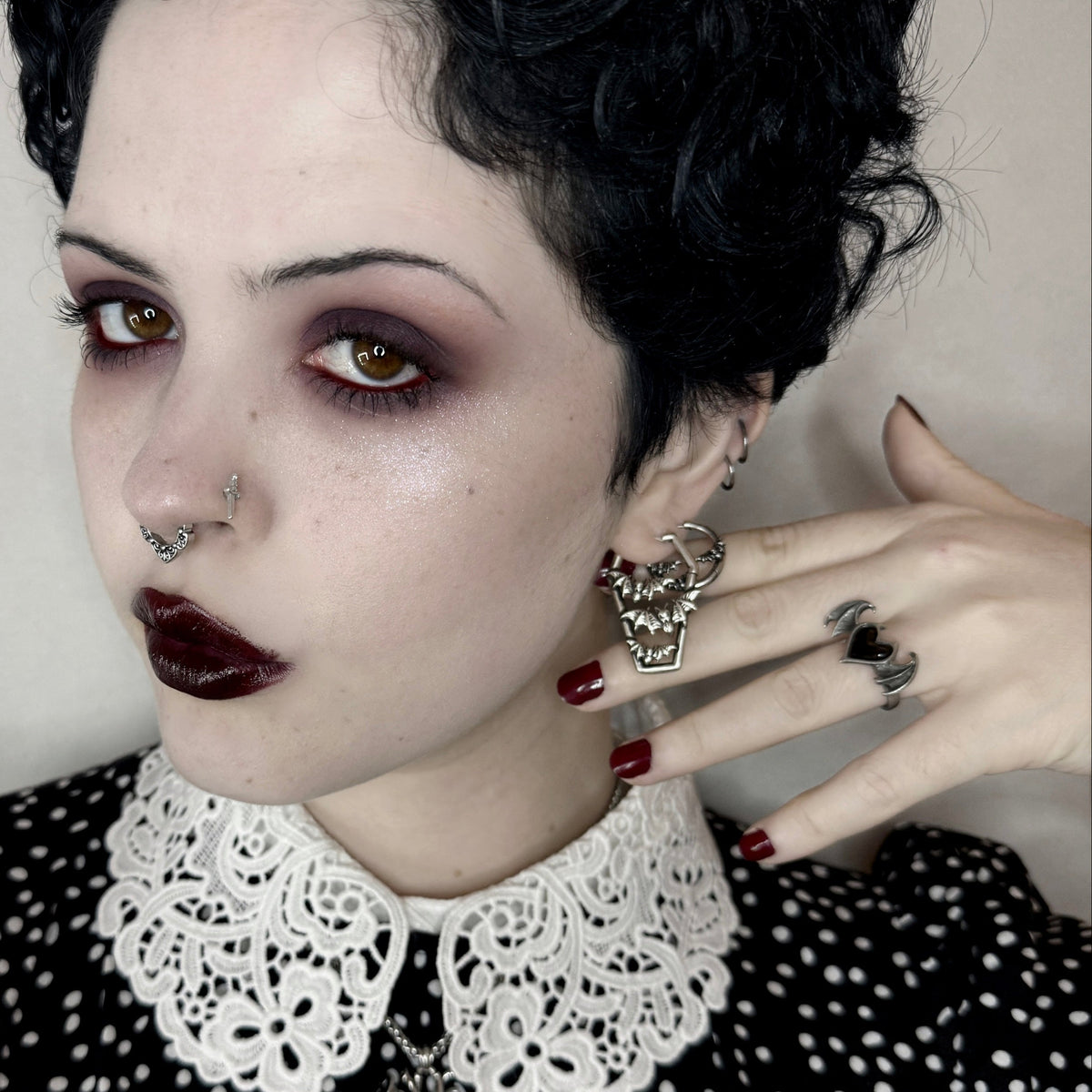 Model with dark makeup wearing a silver-tone coffin-shaped bat charm earring and matching rings