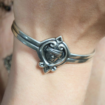 Close-up of an antiqued silver-tone Veiled Seer Cuff Bracelet worn on the wrist, highlighting the raised blindfolded face centerpiece.