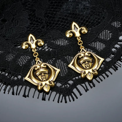 Gold-tone Veiled Seer Drop Earrings displayed as a pair against black lace on a dark reflective surface.