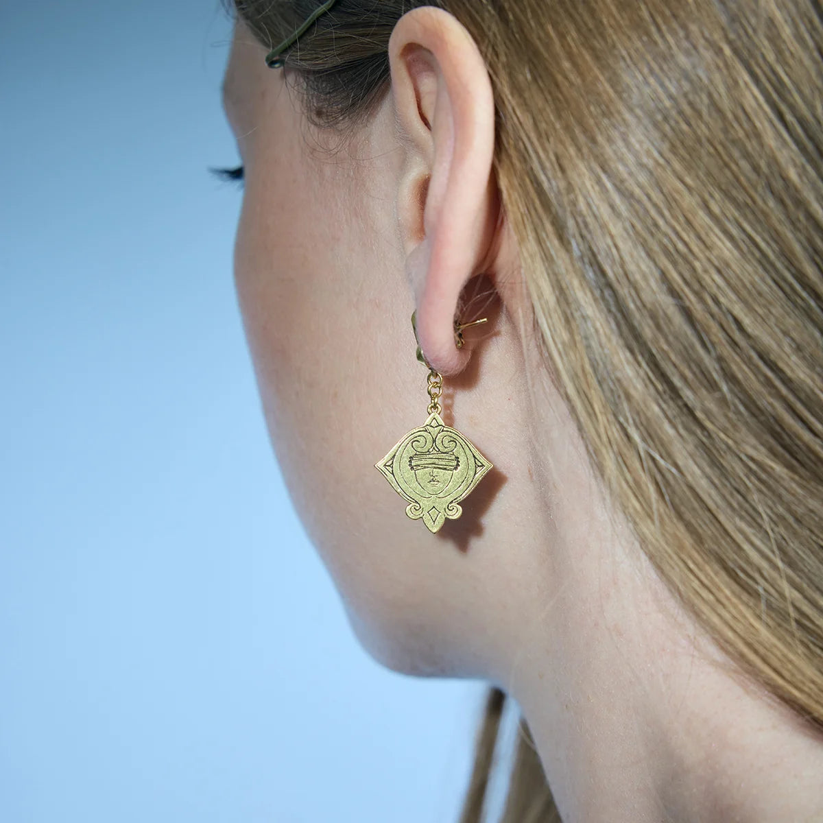 Rear-side portrait showing a gold-tone Veiled Seer Drop Earring and its gently suspended eye-shaped medallion.